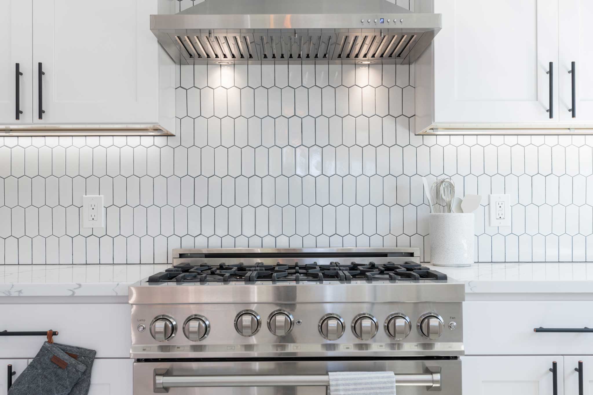 Modern kitchen details of white granite counter, gas stove, and white tile backsplash.