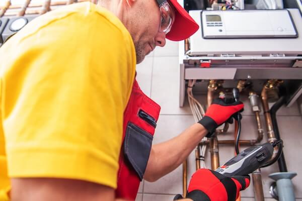 Professional Caucasian Plumber Checking Water Heater Gas Pressure to Make Sure There Are No Leaks. Heating Equipment Maintenance Theme. tankless water heater